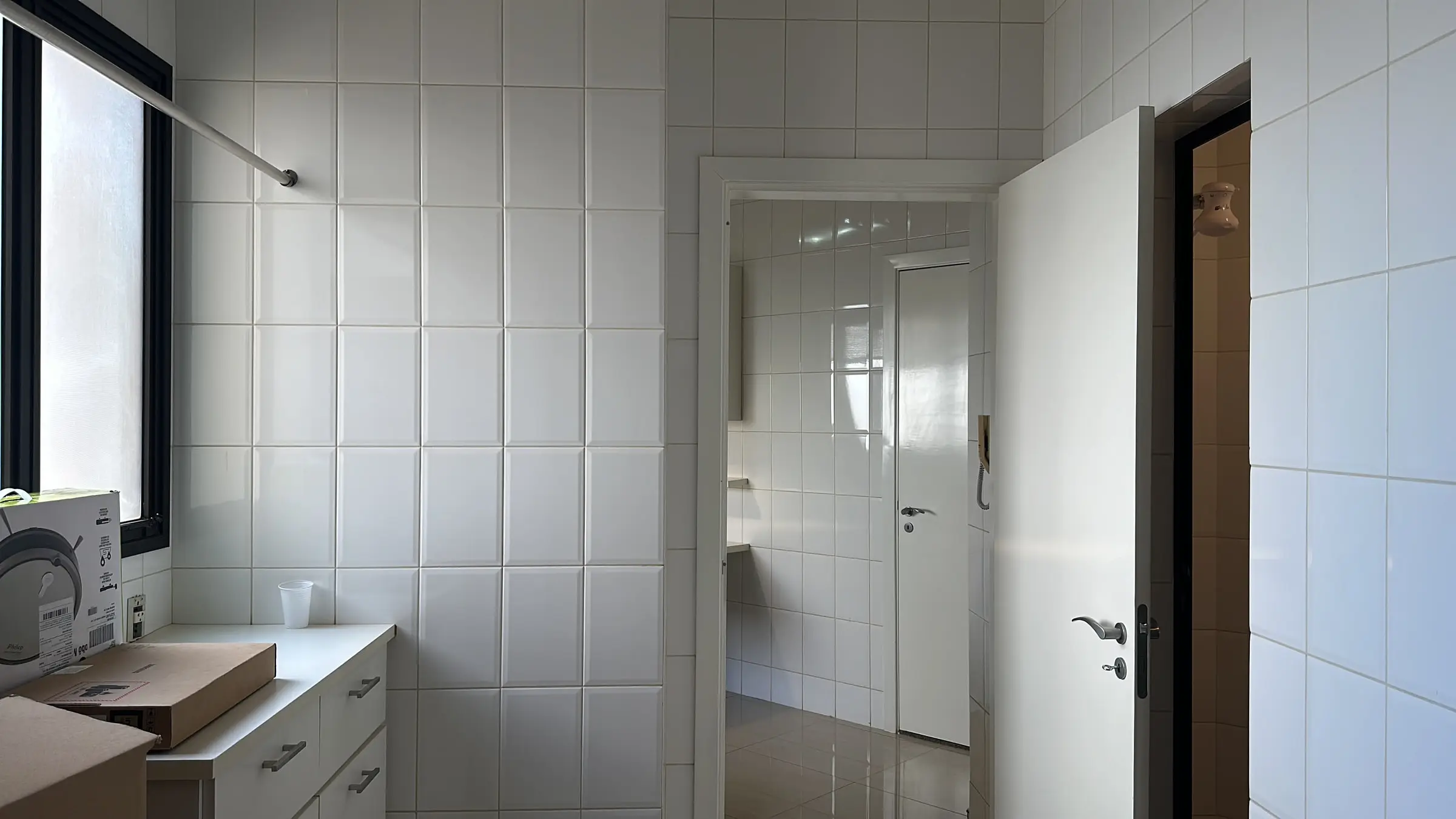 Área de serviço do apartamento revestida em azulejo branco, com bancada e acesso a outros ambientes