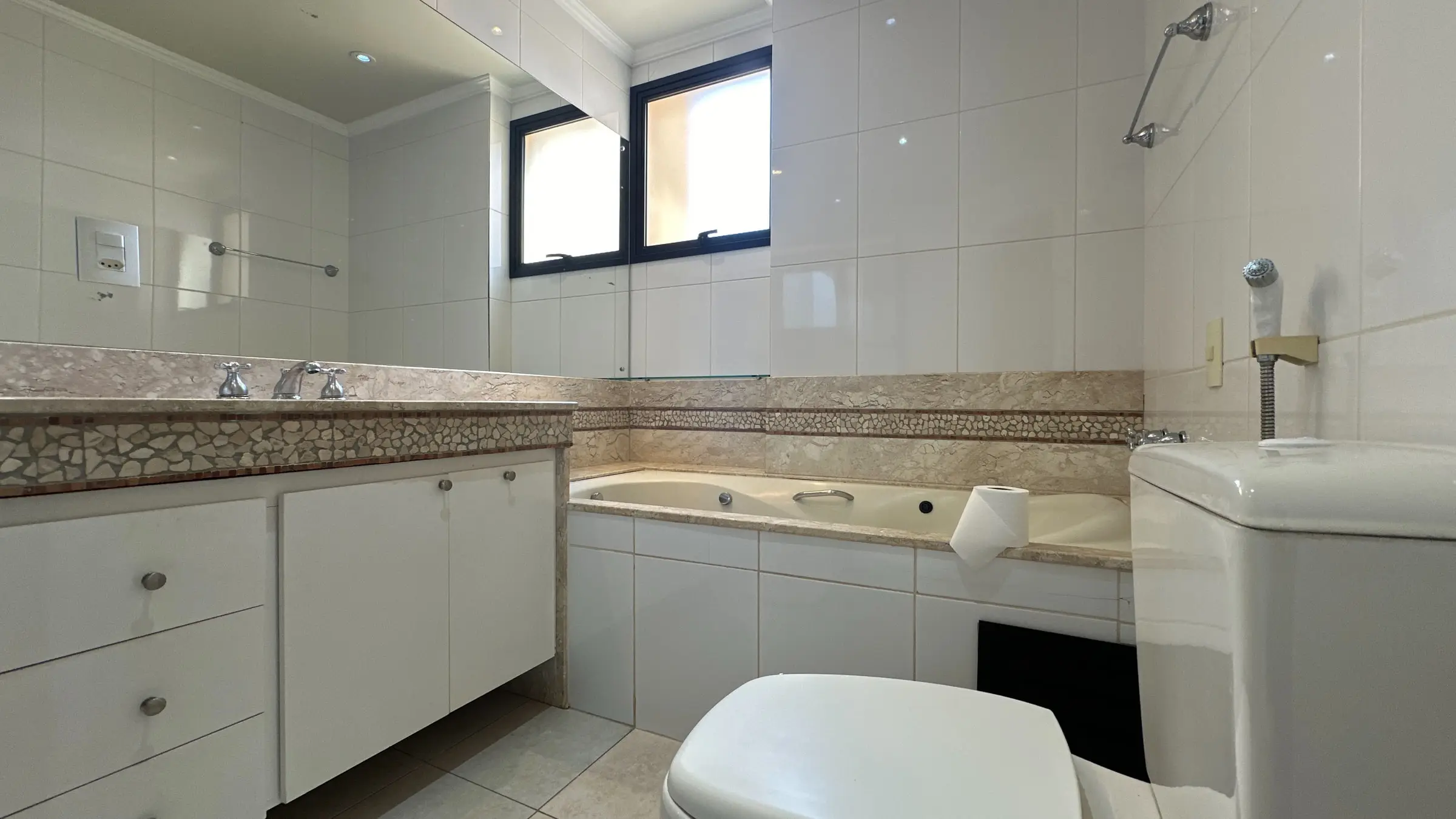 Banheiro do apartamento com banheira de hidromassagem, bancada em pedra e gabinete embutido