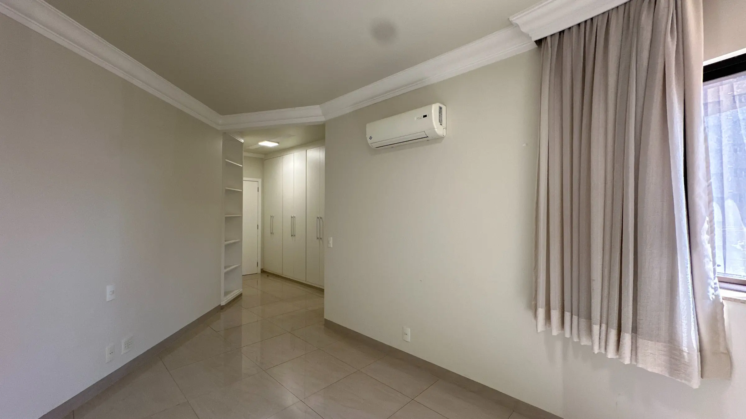 Dormitório do apartamento com aparelho de ar-condicionado e cortinas claras