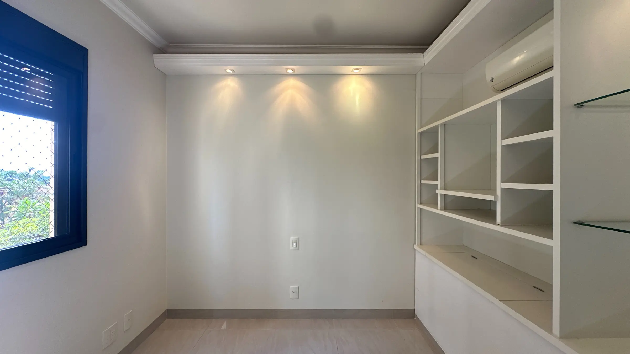 Dormitório do apartamento com estante de marcenaria, iluminação embutida e ar-condicionado