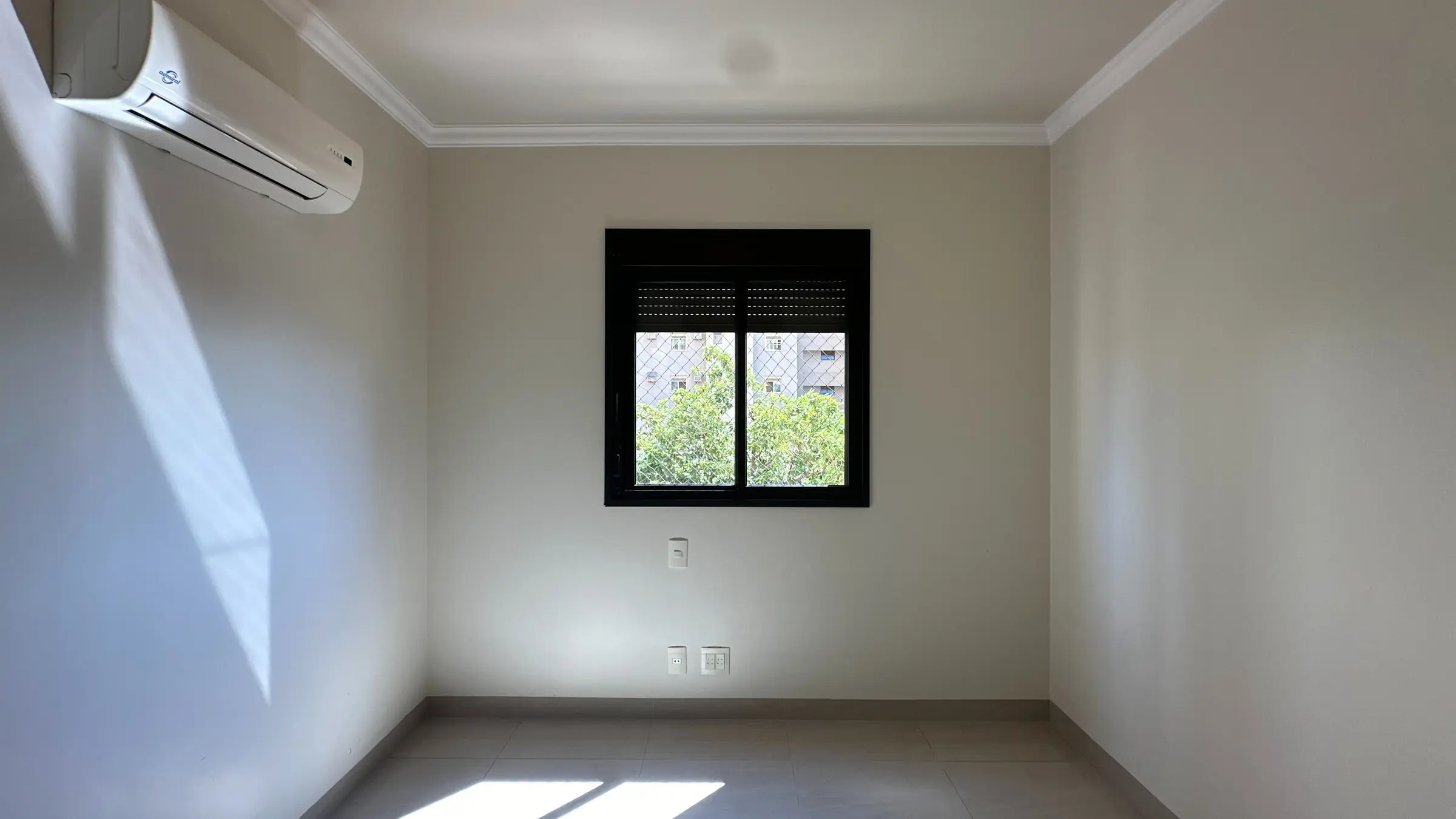 Dormitório vazio do apartamento com janela voltada para área arborizada