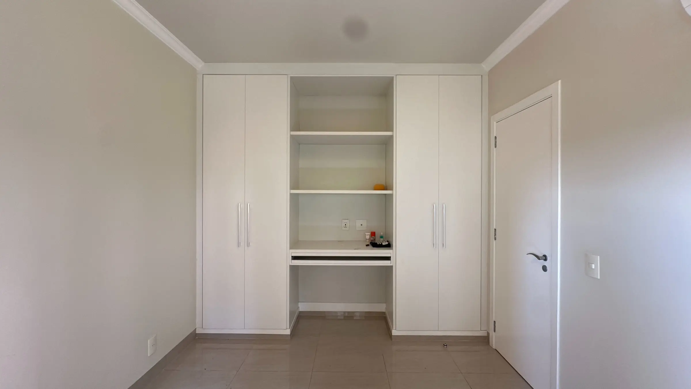 Dormitório do apartamento com armário embutido branco e prateleiras