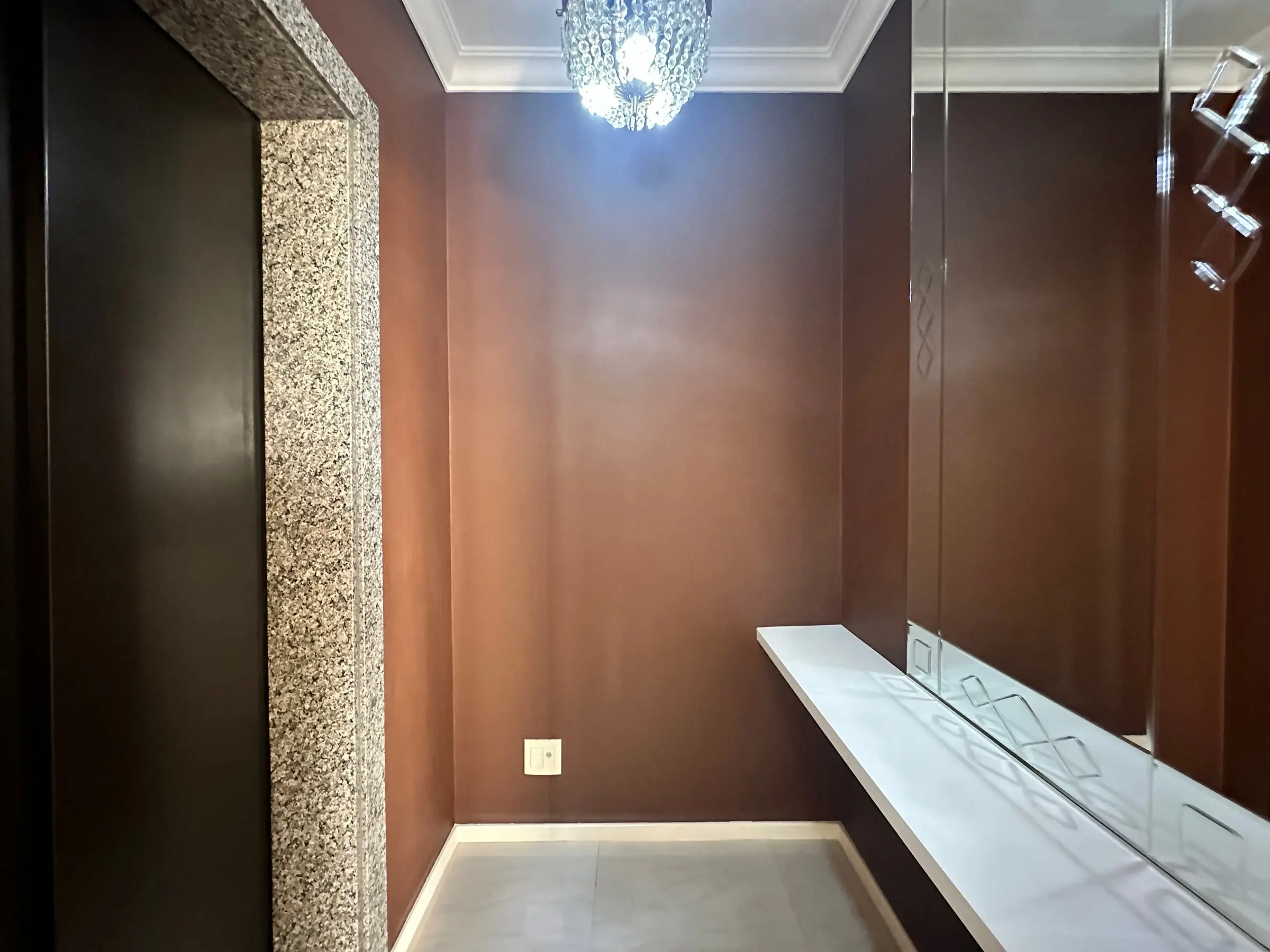 Hall de entrada privativo do apartamento, com moldura em granito, espelho e luminária de cristal