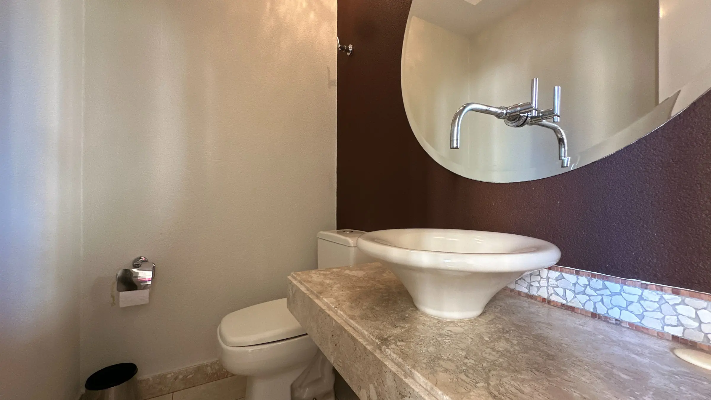 Lavabo do apartamento com cuba de apoio, bancada em pedra e espelho redondo