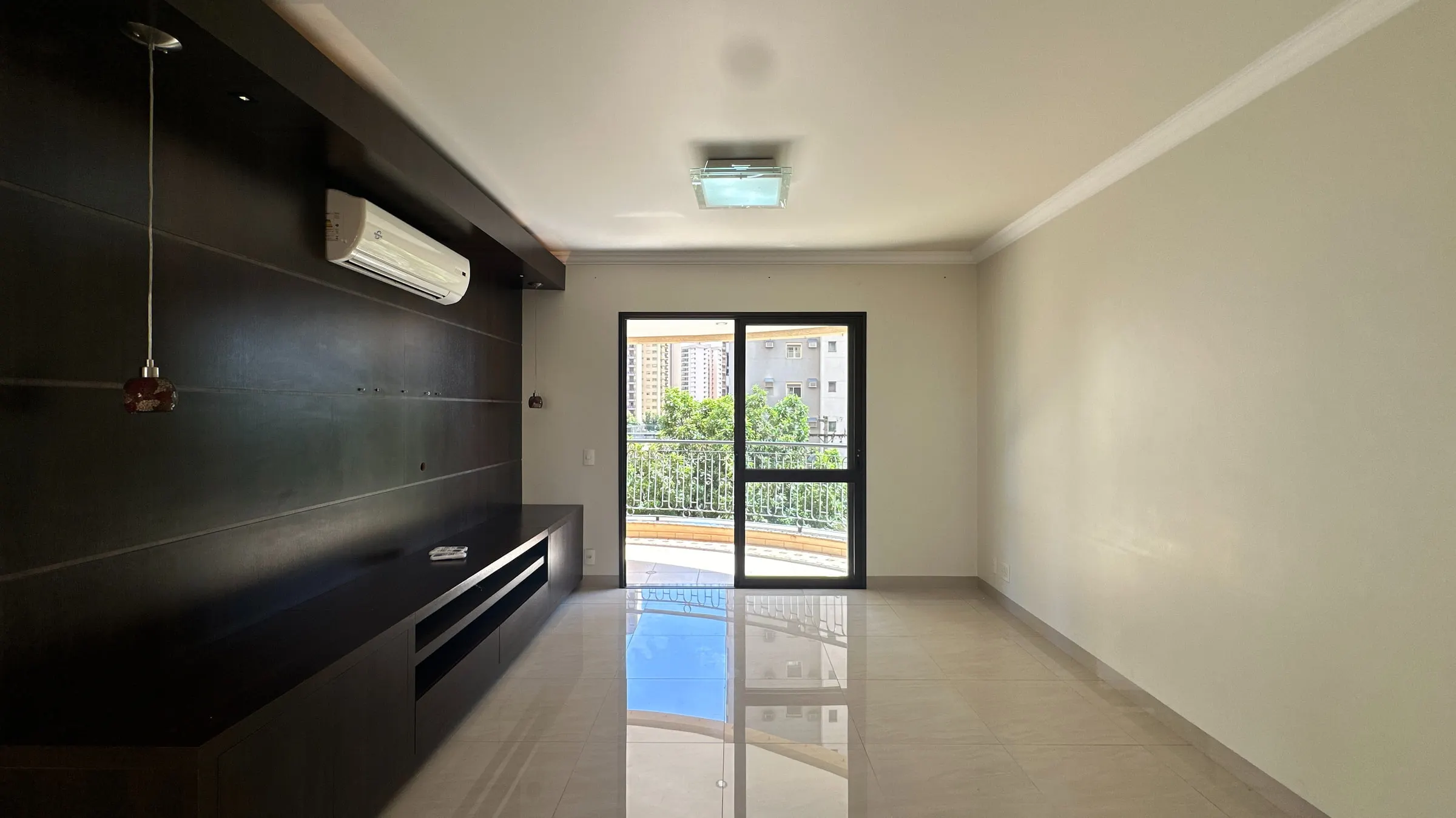 Sala de estar ampla do apartamento na João Fiúsa com painel de madeira escura e porta de vidro para a varanda