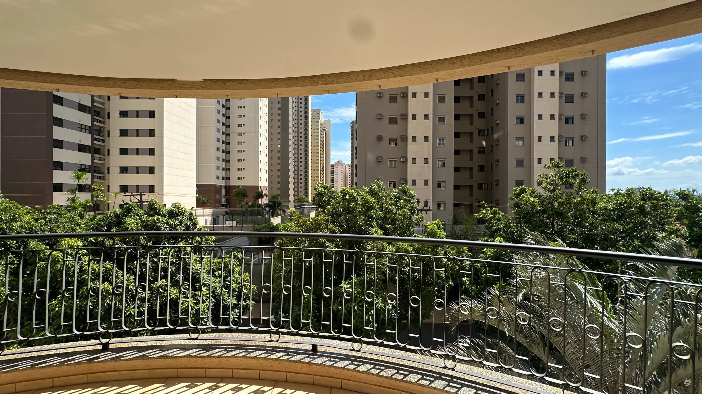 Varanda curva do apartamento com guarda-corpo em ferro e vista para prédios vizinhos e árvores